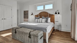 A bedroom with a large bed, a nightstand, a wicker chest, and a window. - Waterfront 4-bedroom house on Topsail Island. Private sandbar/bring your boat! (Topsail Beach)