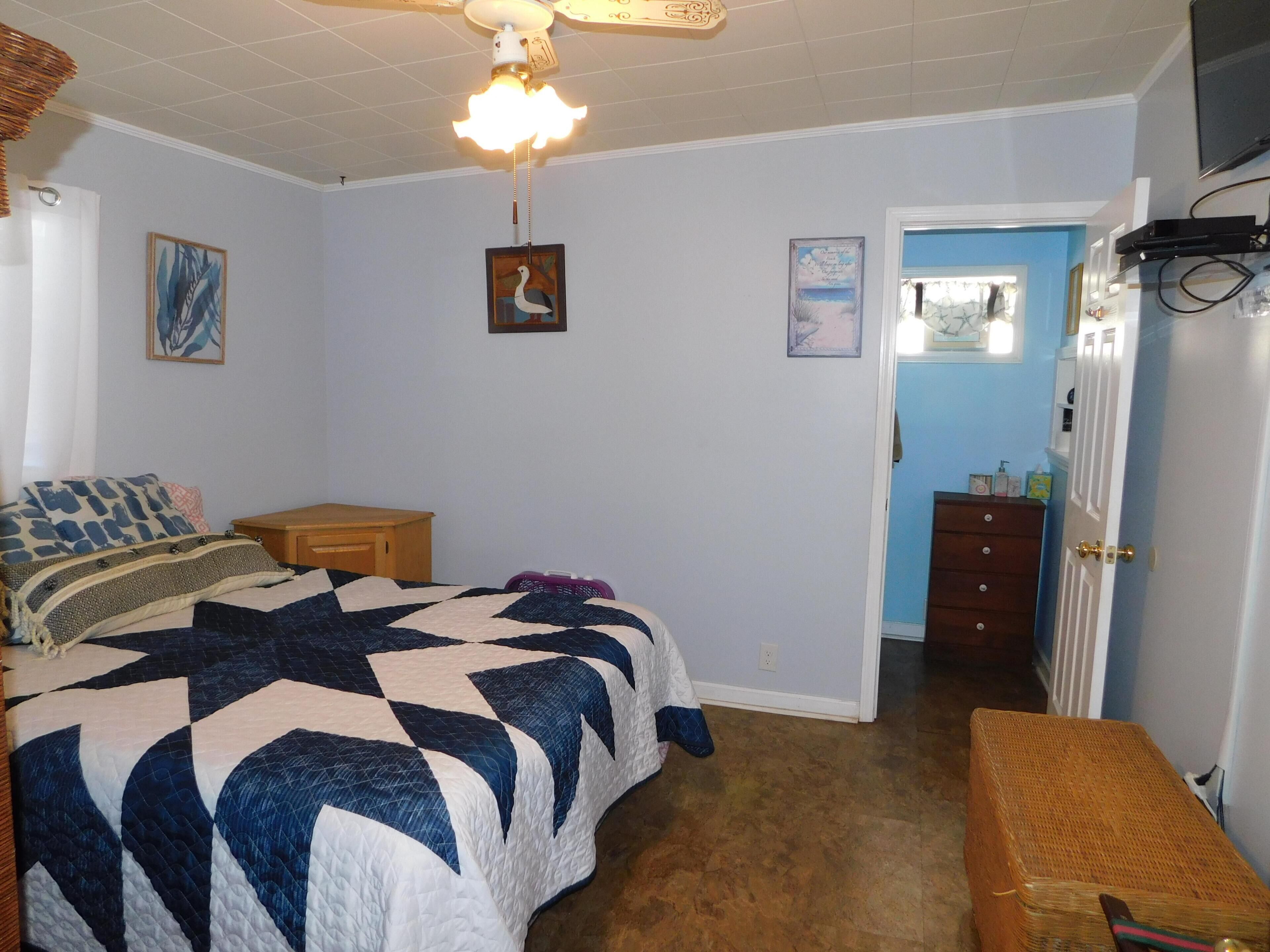 Een slaapkamer met een bed, een houten bankje, een dressoir, een deur en een plafondventilator.