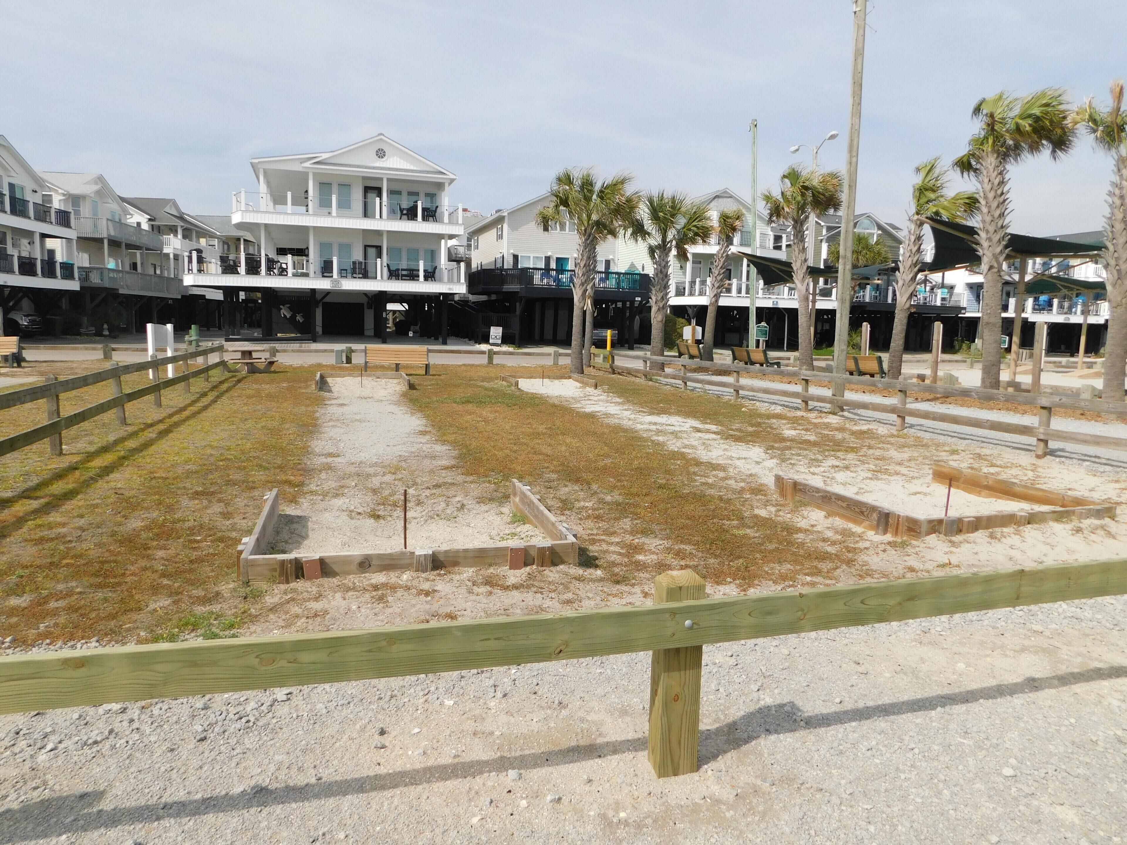 A beachfront property with a large building, a sandy area with wooden structures, and palm trees.
