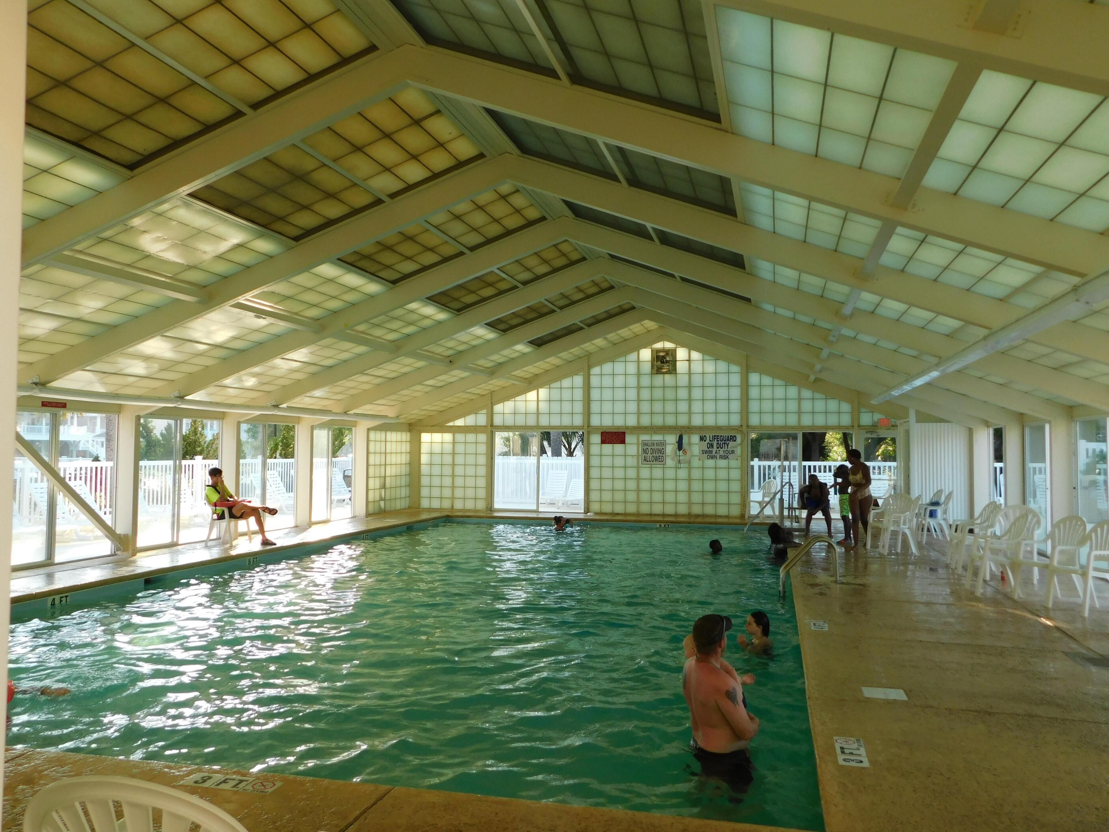 An indoor swimming pool with clear water, a tiled floor, and a high ceiling with skylights.