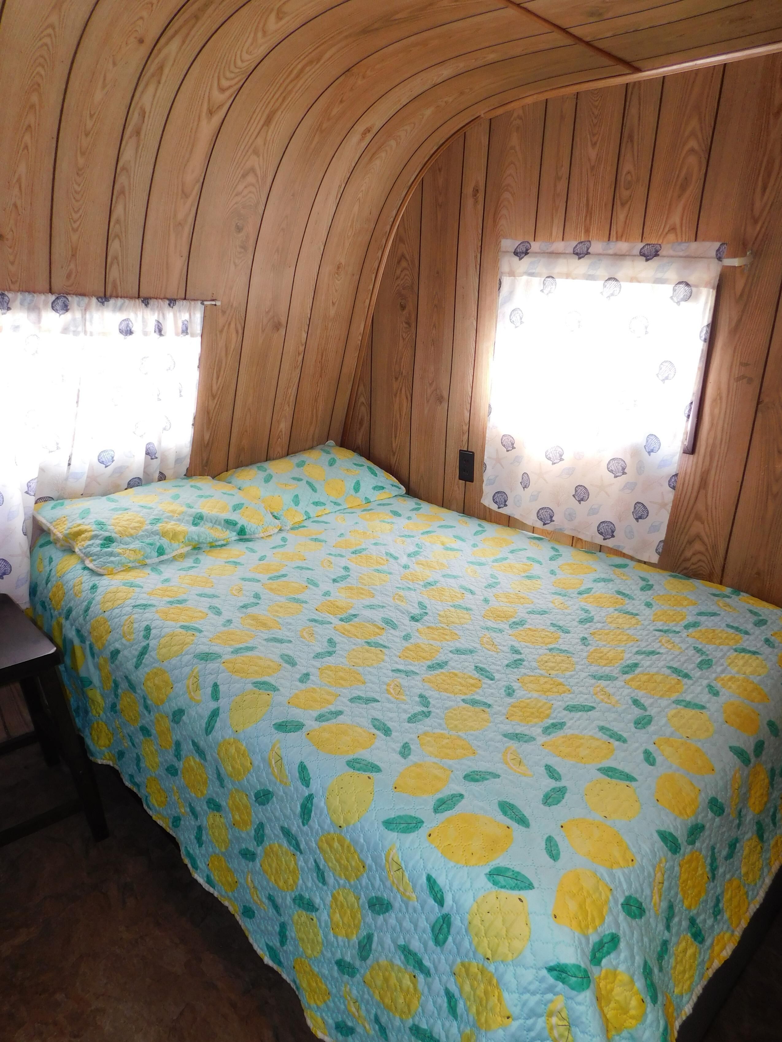 Een kleine, knusse kamer met een gebogen houten plafond, een enkel bed met een bedspreide met citroenmotief, en twee ramen met gordijnen.
