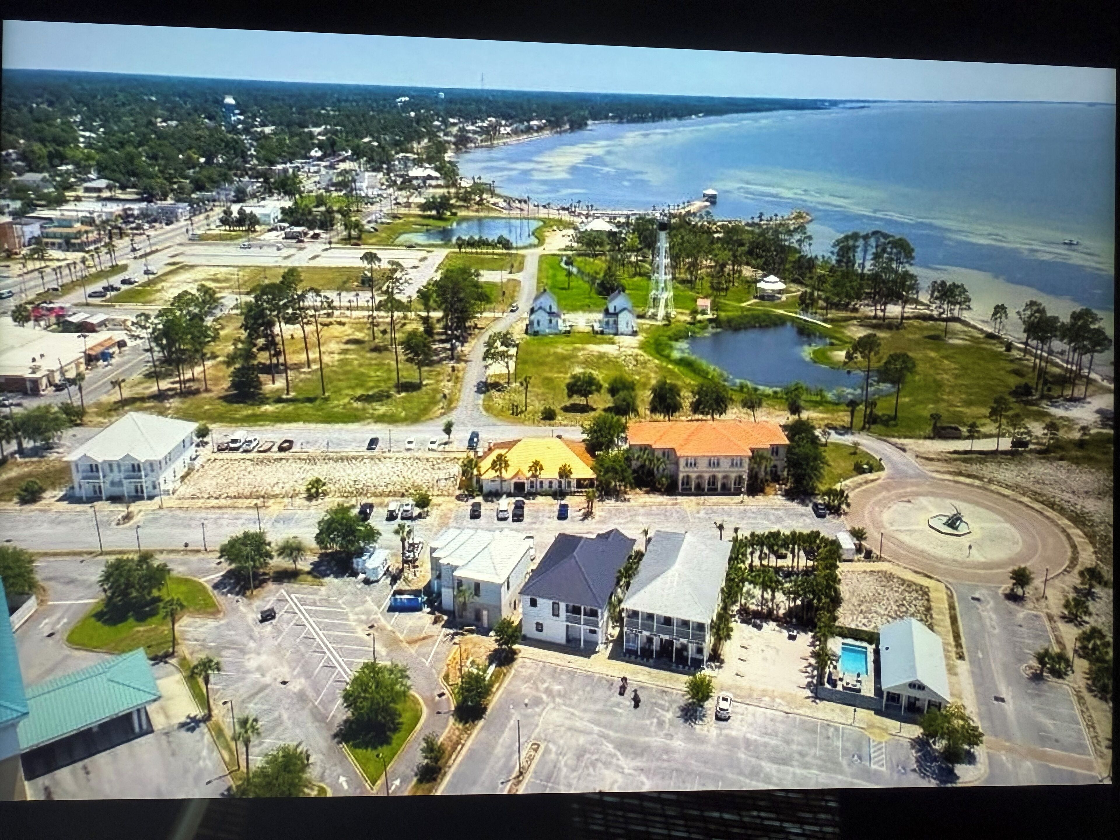 Vista aérea de un pueblo costero con una combinación de edificios residenciales y comerciales, un puerto deportivo y una extensa masa de agua.