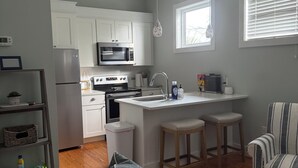 A modern kitchen with white cabinets, a built-in oven, and a microwave. There is a small island with stools, a window with blinds, and a ceiling light fixture. - Awesome  condo in The Marina. At Port St. Joe. 
 Bay views, exciting night life (Port St. Joe)