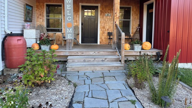 Ein Holzhaus mit einem 'WELCOME'-Schild, einer Veranda mit Stufen und Kürbissen.