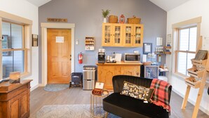 Ein gemütliches Wohnzimmer mit einer schwarzen Couch, Holzschränken und einer Küchenzeile mit Mikrowelle und Kaffeemaschine.