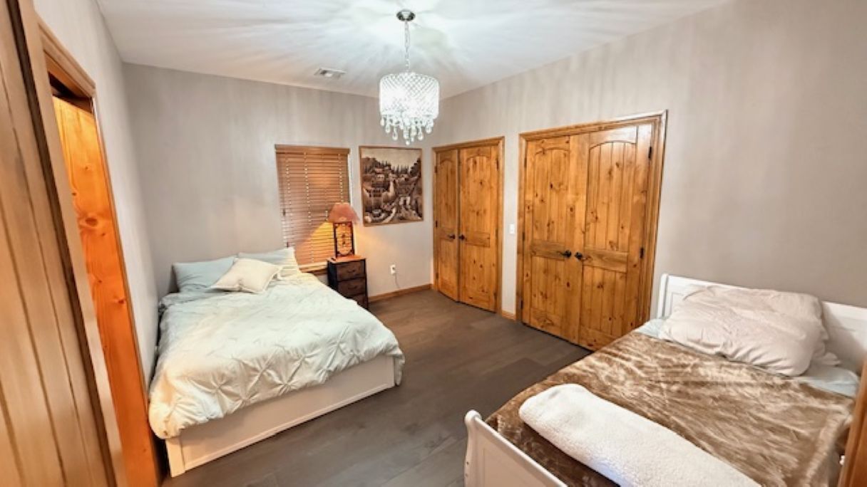 Une chambre avec deux lits, des armoires en bois, un lustre et un tableau au mur.