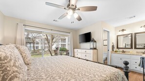 A bedroom with a large bed, a ceiling fan, a TV, a dresser, and a bathroom with a mirror and sink. - Recently Updated 2 Bedroom Condo in Pointe Royale Golf Village with King Beds (Branson)