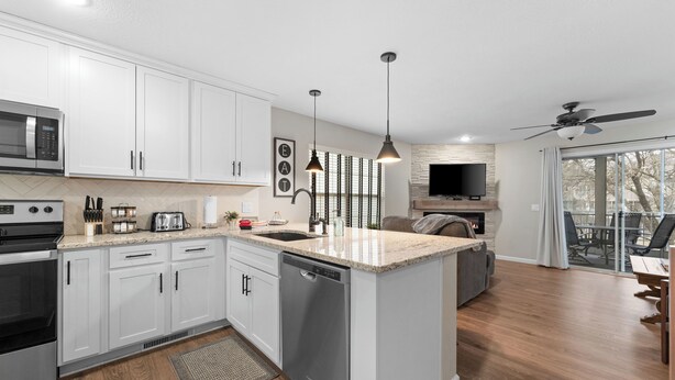 A modern kitchen with white cabinets, a dishwasher, and a built-in microwave. There is a dining area with a table and chairs, and a ceiling fan. - Recently Updated 2 Bedroom Condo in Pointe Royale Golf Village with King Beds (Branson)