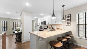 A modern kitchen with white cabinets, a granite island with bar stools, and pendant lighting. - Recently Updated 2 Bedroom Condo in Pointe Royale Golf Village with King Beds (Branson)