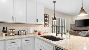 A modern kitchen with white cabinets, a granite countertop, a built-in dishwasher, a sink, a toaster, and a hanging pendant light. - Recently Updated 2 Bedroom Condo in Pointe Royale Golf Village with King Beds (Branson)