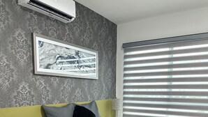 Een moderne slaapkamer met een bed, een nachtkastje met een plant, een wandairconditioner en een raam met zonwering.