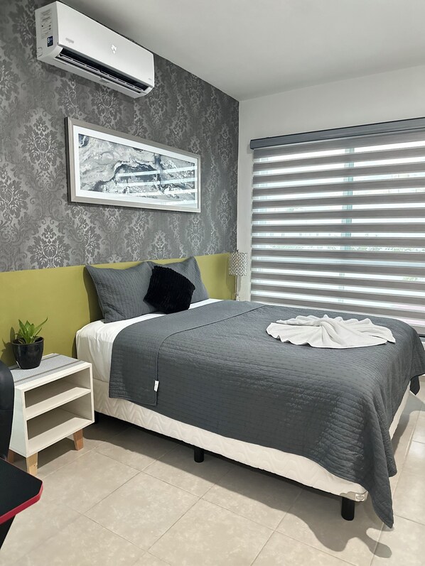 A modern bedroom with a bed, a bedside table with a plant, a wall-mounted air conditioner, and a window with blinds. - Casa Gran Santa Fe, 25 minutes from Playa Lobster Beach in the Cancun Hotel Zone. (Cancún)