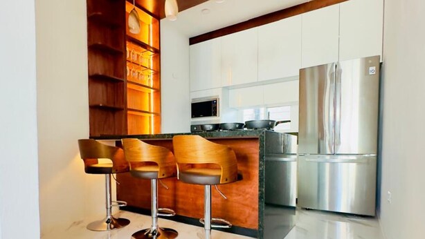 Een moderne keuken met een centraal eiland, een paar barkrukken, roestvrijstalen apparatuur en houten planken.