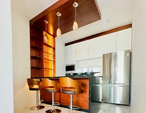 A modern kitchen with a central island, bar stools, stainless steel appliances, and wooden shelving. - Casa Gran Santa Fe, 25 minutes from Playa Lobster Beach in the Cancun Hotel Zone. (Cancún)