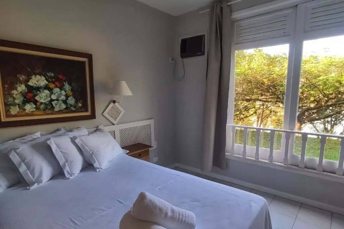 Une chambre d’hôtel avec un grand lit, un tableau au mur, une télévision et un balcon donnant sur la verdure.