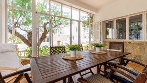 A wooden dining table with chairs, potted plants, and a view of trees and buildings through large windows.