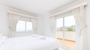 A hotel room with a large bed, two windows with curtains, and a view of the outside.
