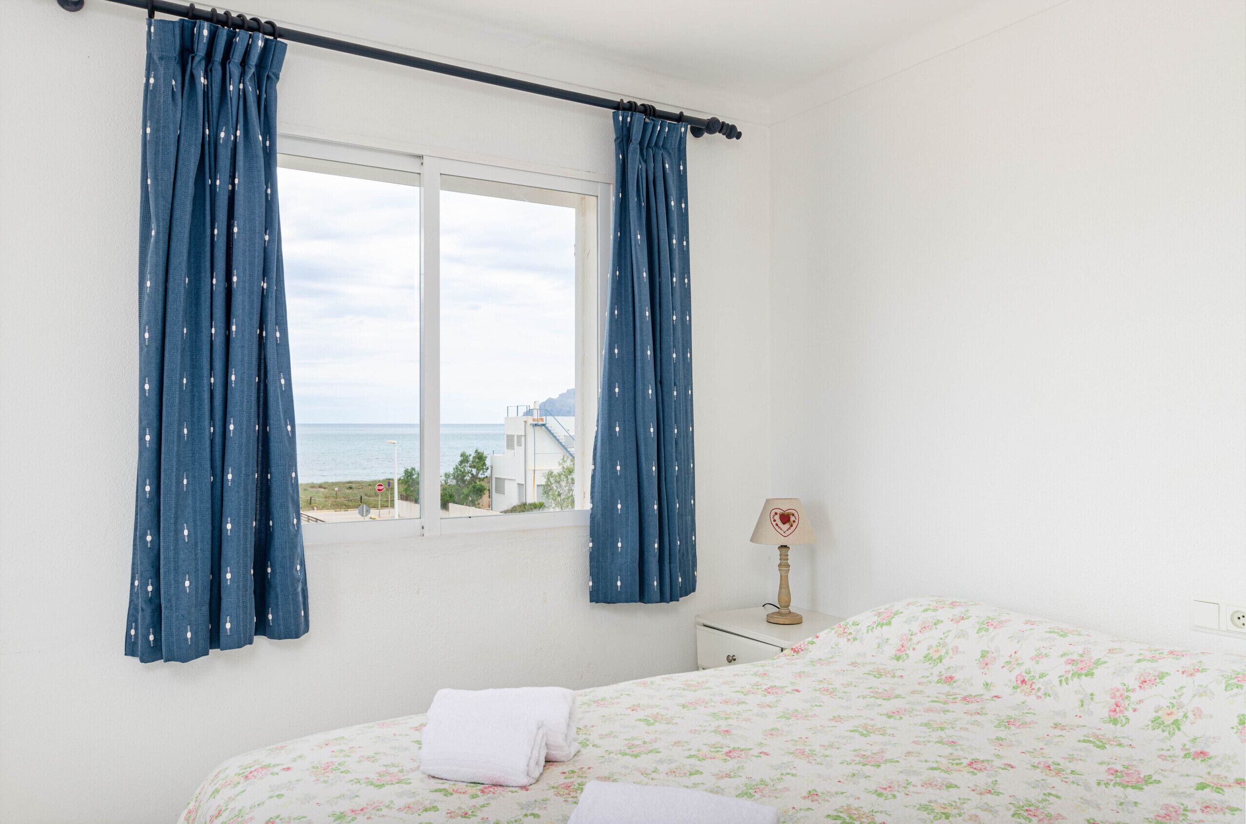 A bedroom with a bed, a nightstand, a lamp, and a window with curtains.