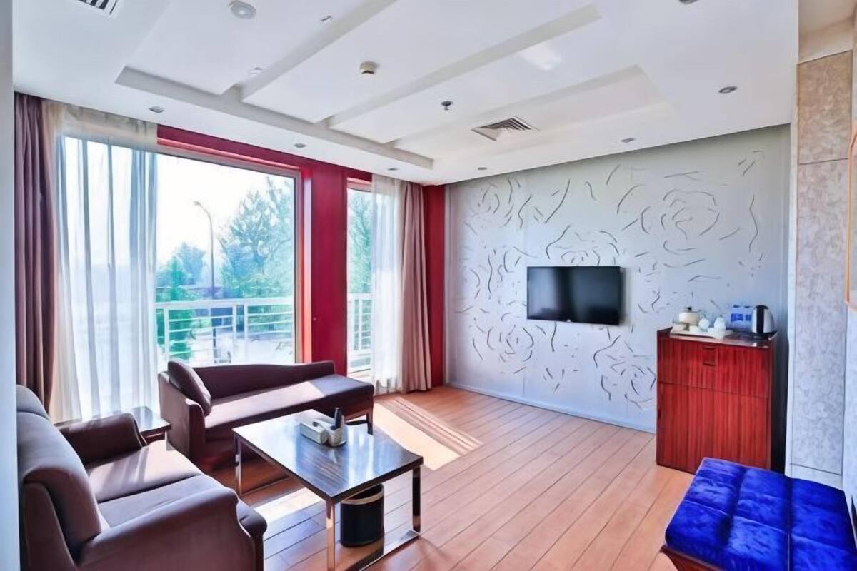 Ein modernes Wohnzimmer mit Sofa, Couchtisch, einem an der Wand montierten Fernseher und einem Balkon mit Vorhängen.