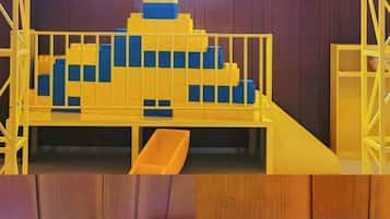 Un espace de jeux avec une structure colorée jaune et bleue, un toboggan et un petit espace clos.