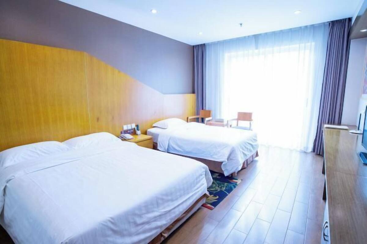 Ein Hotelzimmer mit zwei Betten, einem Schreibtisch, einem Stuhl und einem großen Fenster mit Vorhängen.