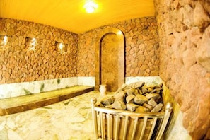 Una habitación con paredes de piedra, un banco, una pequeña piscina y un estante de metal con rocas.