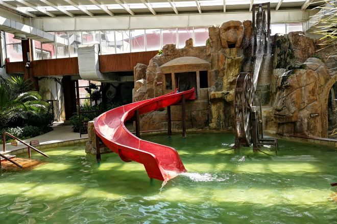 An indoor water slide with a red slide, a rock formation backdrop, and a pool area.