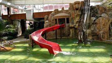 An indoor water slide with a red slide, a rock formation backdrop, and a pool area.