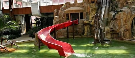 An indoor water slide with a red slide, a rock formation backdrop, and a pool area.