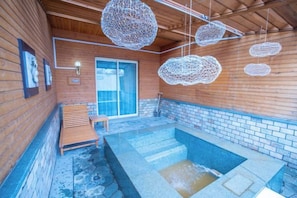 A wooden cabin with a stone hot tub, wooden benches, and hanging light fixtures. - Nangong Hot Spring Health Hotel (Beijing)