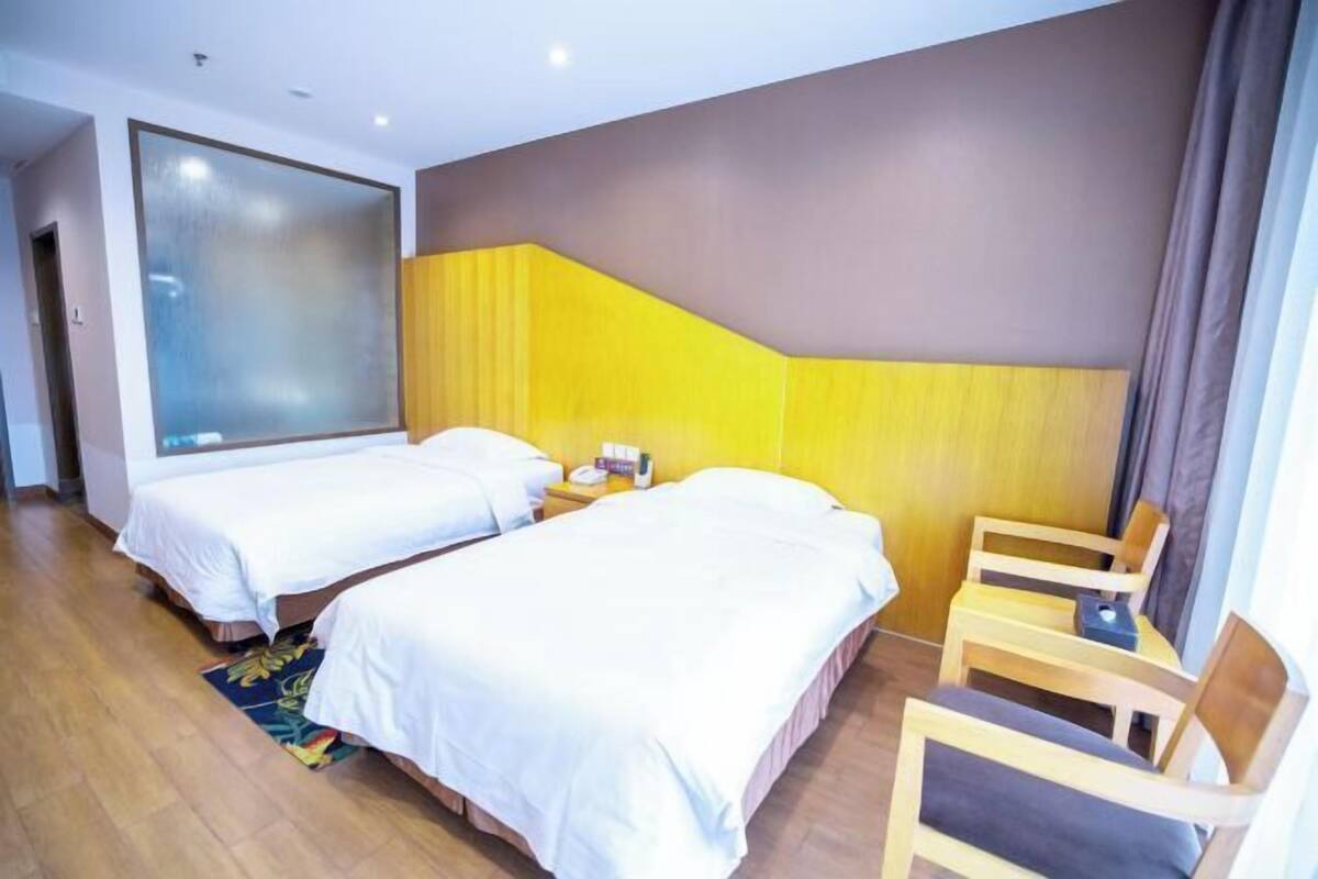Ein Hotelzimmer mit zwei Betten, einem Holzsessel, einem kleinen Tisch und einem großen Fenster.