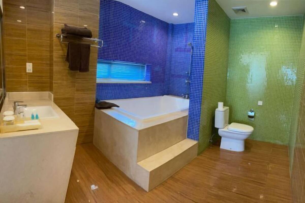Ein modernes Badezimmer mit Badewanne, Toilette und Waschbecken, mit blau- und grün schimmernden Mosaikfliesen.