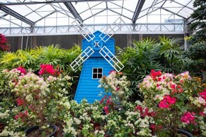 A blue windmill structure surrounded by lush greenery and flowering plants inside a greenhouse. - Nangong Hot Spring Health Hotel (Beijing)