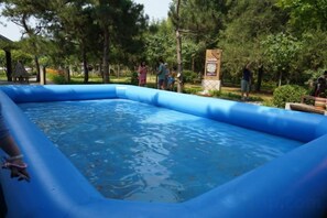 An inflatable pool surrounded by trees and a signboard. - Nangong Hot Spring Health Hotel (Beijing)