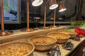 A buffet area with multiple baskets of food, copper serving lamps, and a window with a view.