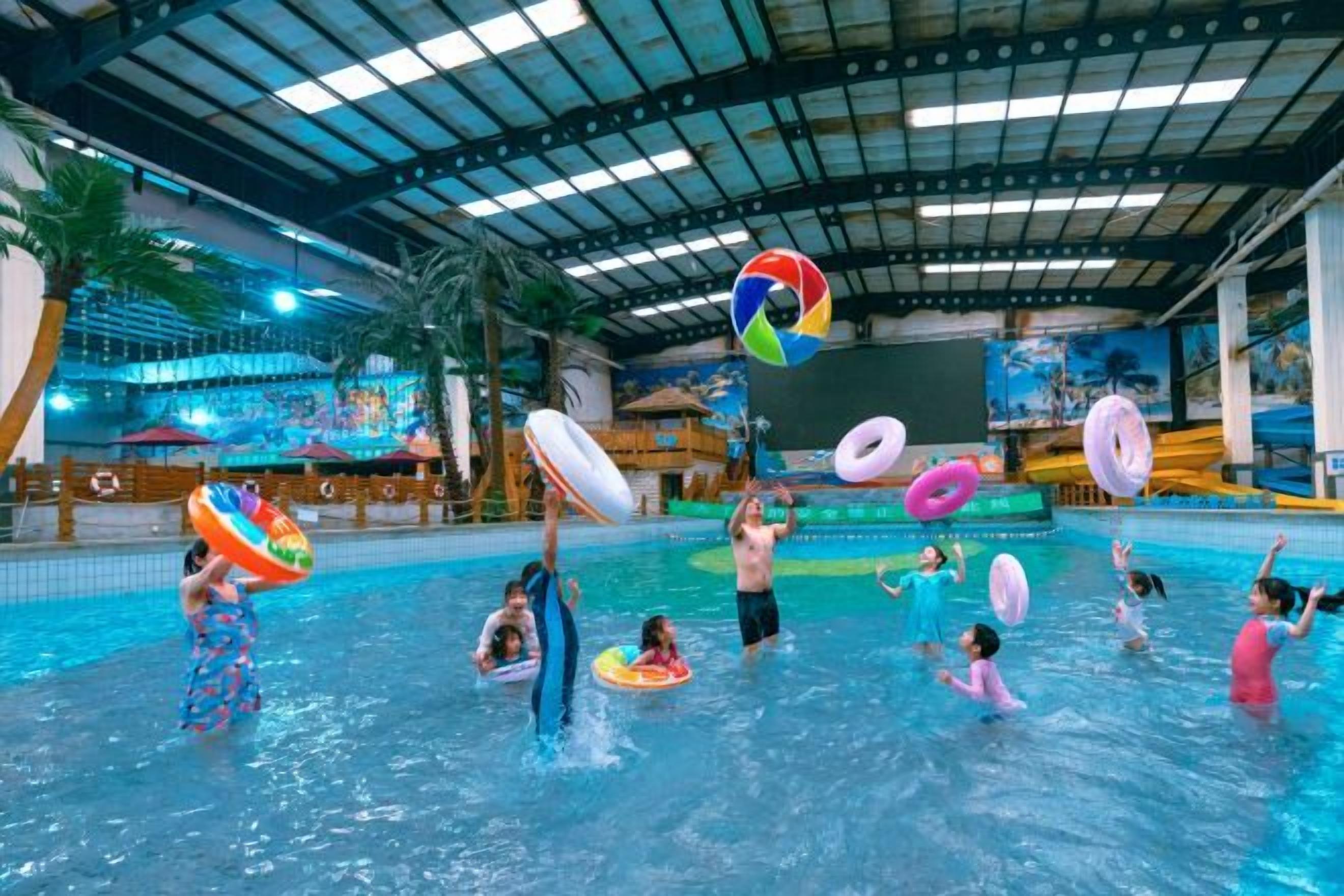 Piscina interna com várias pessoas e boias coloridas.