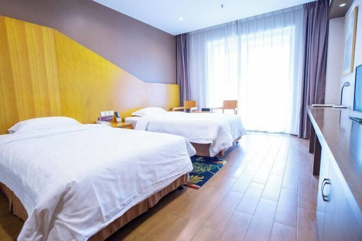 Ein Hotelzimmer mit zwei Betten, einem Schreibtisch, einem Sessel und einem großen Fenster mit Vorhängen.
