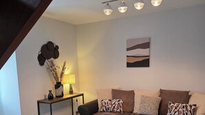 Een moderne woonkamer met een hoekbank, een ronde salontafel, een bijzettafeltje met een lamp en een wandlamp.