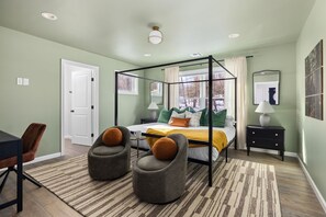 A bedroom with a four-poster bed, two armchairs, a desk, and a nightstand.
