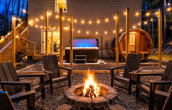 Eine Holzterrasse mit Feuerstelle, Sitzgelegenheiten im Freien und Lichterketten.