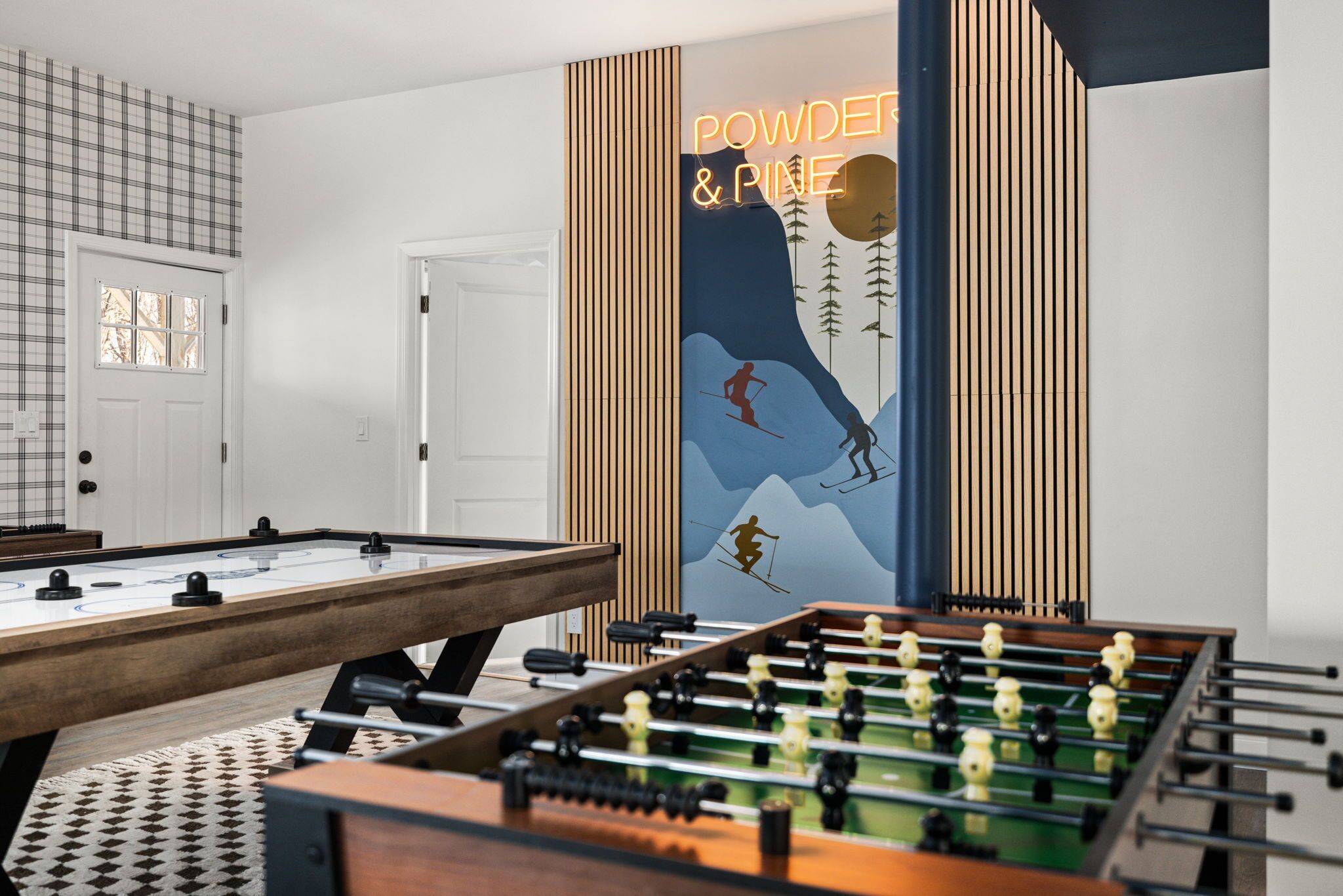 A room with a foosball table, a pool table, and a wall with a ski-themed artwork.