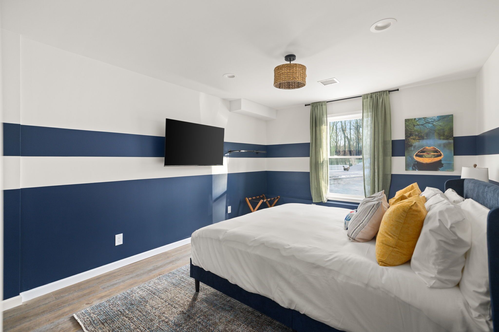 Een slaapkamer met een bed, een flatscreen televisie aan de muur, een raam met gordijnen en een schilderij.