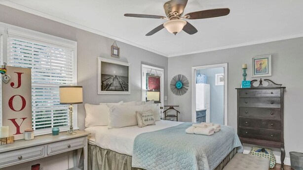 A bedroom with a bed, bedside table, dresser, and a ceiling fan.