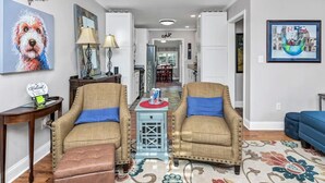 A living room with two armchairs, a coffee table, and a rug. There is a painting of a dog on the wall and another painting of a cityscape.