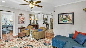 A spacious living room with a blue sofa, two armchairs, a patterned rug, and a ceiling fan.