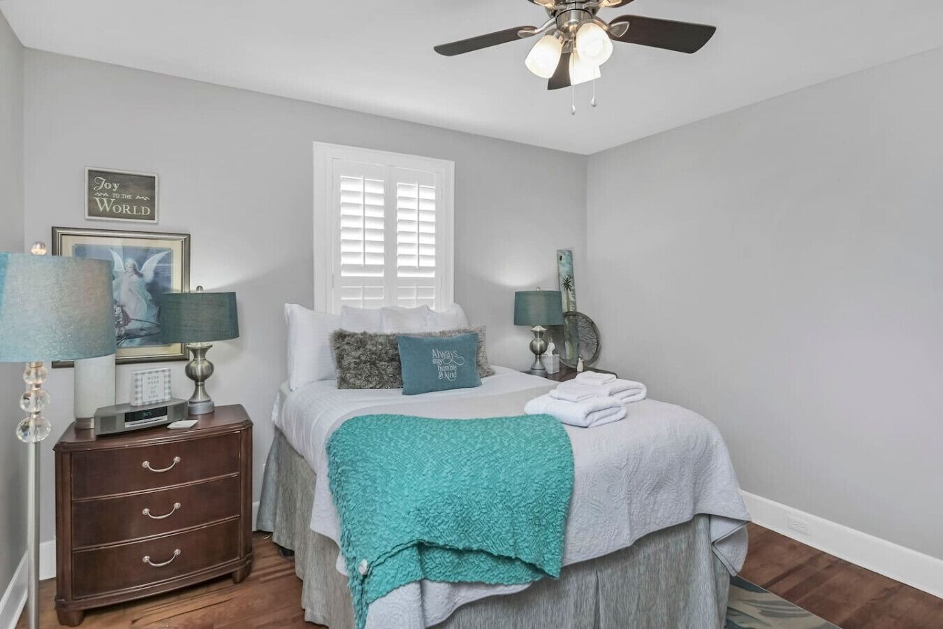 A bedroom with a bed, a nightstand, a dresser, a ceiling fan, and a window with blinds.