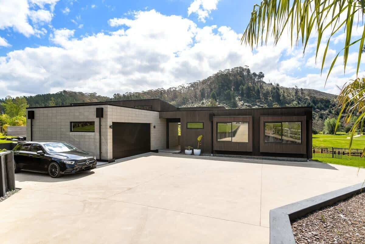 Une maison moderne avec un garage, une allée et une vue sur les montagnes en arrière-plan.