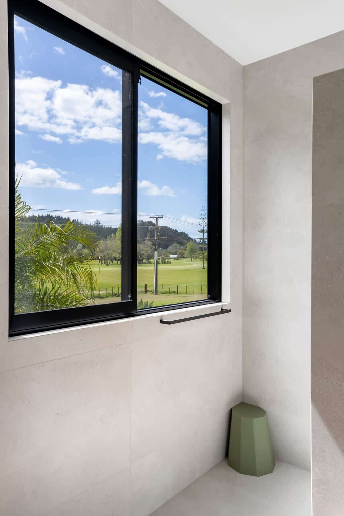 A room with a large window, a green object on the floor, and a view of a green field and trees.