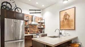 A modern kitchen with a stainless steel refrigerator, a brick backsplash, and a wooden island with stools. - Downtown Barnwood Condo. WSTR-21-00029 (Whitefish)