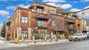 A multi-story building with a rustic wooden facade, large windows, and a street view with parked cars. - Downtown Barnwood Condo. WSTR-21-00029 (Whitefish)